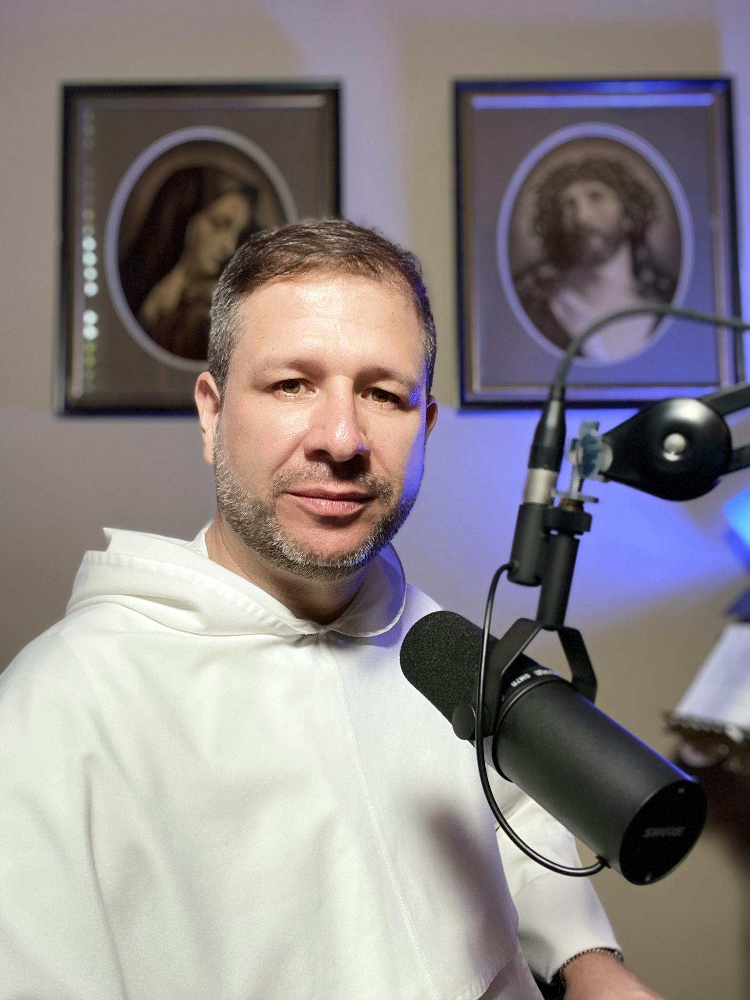 A Catholic friar with a microphone in a religious setting, broadcasting from New Orleans.